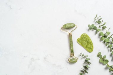 Yeşim silindir ve gua sha taş masajcısı mermer masada.