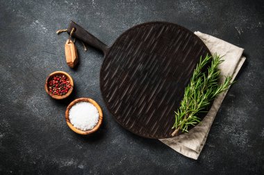 Mutfak aletleri, otlar ve baharatlarla siyah arka planda kesim tahtası. Kopyalama alanı olan üst görünüm.