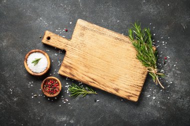 Mutfak aletleri, otlar ve baharatlarla siyah arka planda kesim tahtası. Kopyalama alanı olan üst görünüm.