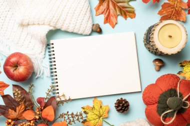 Sonbahar düzlüğü, Şükran Günü konsepti. Düşen yapraklar, not defteri, örgü eşarp ve mavi arka planda ahşap mum..