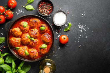 Köfteler siyah tabakta, siyah arkaplanda ve yemek malzemeleri var. Metin için boşluk olan üst görünüm.