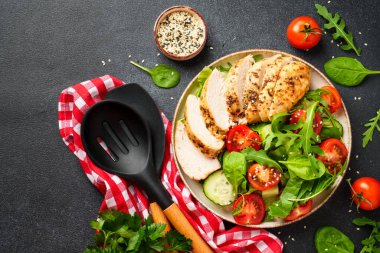 Siyah arka planda tavuk salatası. Izgara tavuk göğsü, domates ve yeşil yapraklar. Tasarım için alanı olan üst görünüm.