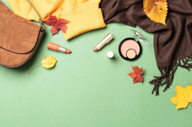 Autumn flat lay background. Warm cloth, bag and cosmetics. Woman cloth and beauty products with fallen leaves.