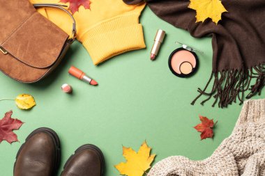 Autumn flat lay background. Warm cloth, bag and cosmetics. Woman cloth and beauty products with fallen leaves.