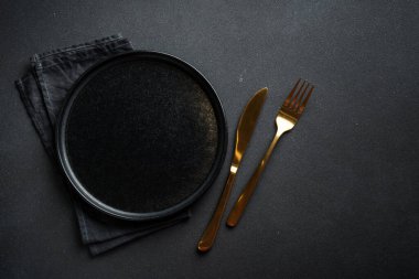 Altın çatal bıçaklı siyah tabak. Modern moda yemekler. Siyah arkaplanda düz uzandı.