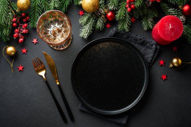 Noel sofrası. Noel yemeği. Siyah arka planda siyah tabaklar, çatal bıçak takımı ve süslemeler. Kopyalama alanı olan düz.