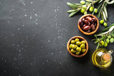 Tahta kaselerde zeytin yağı ve taze zeytin dalları. Siyah arkaplanda üst görünüm.