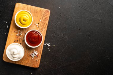 Sos kaseleri - mayonez, hardal, siyah arka planda ketçap. Üst görünüm.