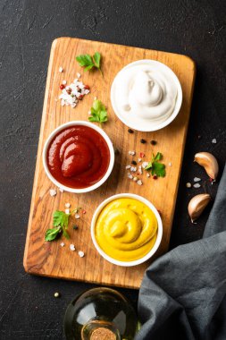 Kesme tahtasında ketçap, mayonez ve hardal var. Üst görünüm, aşçılık arka planı.