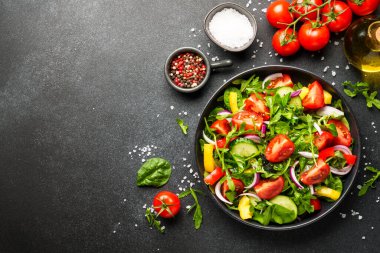 Yeşil yapraklı ve sebzeli taze salata. İçindekilerle birlikte siyah üzerine üstten görünüm.