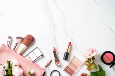 Beyaz mermer arka planda çiçekli ürünler uydur. Kozmetik palet, fırçalar ve rujlar. Kopyalama alanı olan üst görünüm.