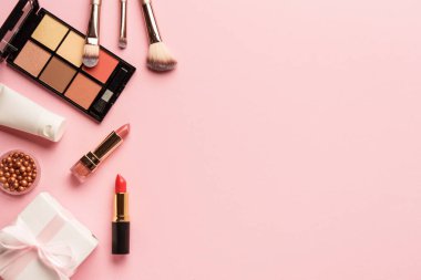 Ürünleri ve hediye kutusunu pembe arka planda hazırla. Göz farı, ruj ve kozmetik fırçalar..