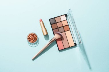 Mavi arka plandaki ürünleri uydur. Kozmetik palet, fırçalar ve ruj. Kopyalama alanı olan üst görünüm.