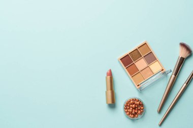 Mavi arka plandaki ürünleri uydur. Kozmetik palet, fırçalar ve ruj. Kopyalama alanı olan üst görünüm.