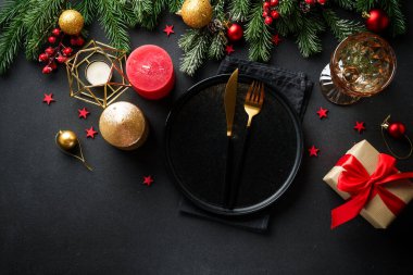 Noel sofrası. Noel yemeği. Siyah arka planda siyah tabaklar, çatal bıçak takımı ve süslemeler. Kopyalama alanı olan düz.