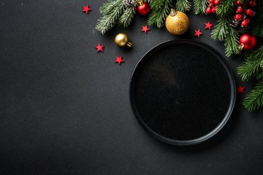 Noel sofrası. Noel yemeği. Siyah arka planda siyah tabaklar, çatal bıçak takımı ve süslemeler. Kopyalama alanı olan düz.