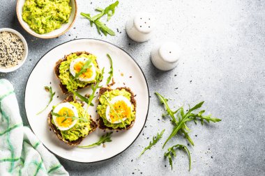 Avocado sandwich. Whole grain bread with avocado and boiled eggs with arugula. Top view on white background.