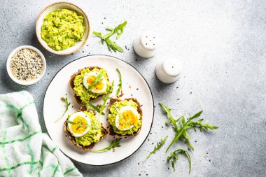 Avocado sandwich. Whole grain bread with avocado and boiled eggs with arugula. Top view on white background.