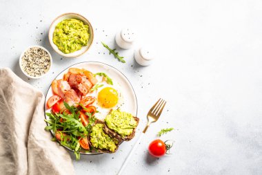 Becon, eggs, toast with avocado and fresh salad. Healthy food, paleo diet. Top view on white kitchen table.