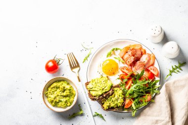 Healthy breakfast or lunch. Beacon, eggs, toast with avocado and fresh salad. Top view on white kitchen table.