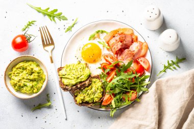 Healthy breakfast or lunch. Becon, eggs, toast with avocado and fresh salad. Top view on white kitchen table.