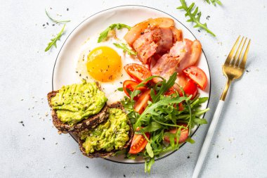 Healthy breakfast or lunch. Becon, eggs, toast with avocado and fresh salad. Top view on white kitchen table.