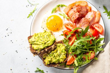 Healthy breakfast or lunch. Becon, eggs, toast with avocado and fresh salad. Top view on white kitchen table.