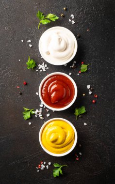 Sos kaseleri - mayonez, hardal, siyah arka planda ketçap. Üst görünüm, dikey.