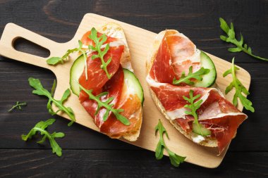 Sandviçleri krem peynirli, jambonlu, salatalıklı ve roka dilimli açın..