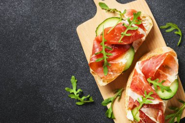 Sandviçleri krem peynirli, jambonlu, salatalıklı ve roka dilimli açın..