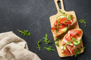 Sandviçleri krem peynirli, jambonlu, salatalıklı ve roka dilimli açın..