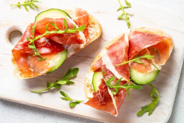 Open sandwiches with cream cheese, prosciutto and arugula at white background. Top view image.