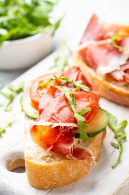 Beyaz arka planda kesme tahtasının üzerinde prosciutto ve roka ile sandviç açın. Resmi kapat.