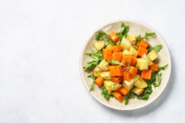 Balkabağı salatası. Sıcak balkabağı, baharatlı patates ve taze roka. Beyaz masadaki üst görünüm.