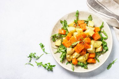 Balkabağı salatası. Sıcak balkabağı, baharatlı patates ve taze roka. Beyaz masadaki üst görünüm.