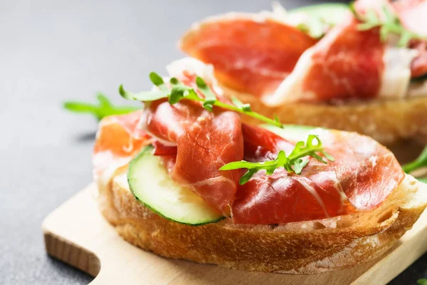 Beyaz arka planda kesme tahtasının üzerinde prosciutto ve roka ile sandviç açın. Resmi kapat.