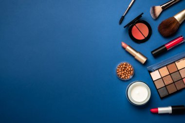 Kış makyajı, kozmetik ürünler. Yüz kremi, makyaj gölgeleri, ruj, mavi arka planda kozmetik fırçalar.