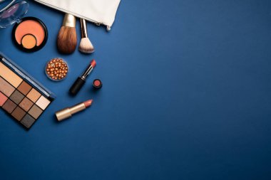 Kış makyajı, kozmetik ürünler. Yüz kremi, makyaj gölgeleri, ruj, mavi arka planda kozmetik fırçalar.