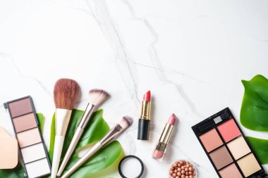 Beyaz mermer arka planda çiçekli ürünler uydur. Kozmetik palet, fırçalar ve rujlar. Kopyalama alanı olan üst görünüm.