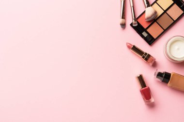 Göz farı paleti, fosforlu kalem, krem, ruj ve kozmetik fırçalar. Pembe arka planda düz uzandı.