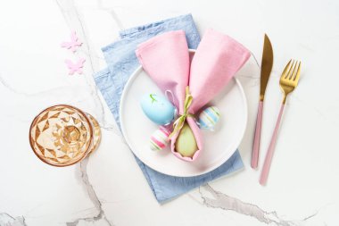 Beyaz tabak, altın çatal bıçak, şarap kadehi ve renkli paskalya yumurtası. Kopyalama alanı olan üst görünüm.