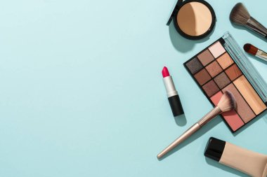 Mavi arka plandaki ürünleri düzleştirin. Kozmetik palet, fırça, krem ve ruj.