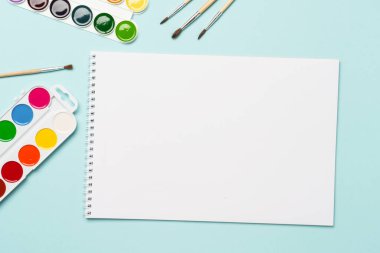 Eskiz kitabı, suluboya resimler ve mavi arka planda fırçalar. Düz görünüm.