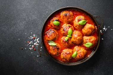 Domates soslu jöleli köfteler siyah zemin üzerinde demir tabakta. Metin için boşluk olan üst görünüm.