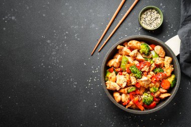 Kızartma tavuk ve sebzeler ve siyah arka planda susam. Asya mutfağı. Tasarım için alanı olan üst görünüm.