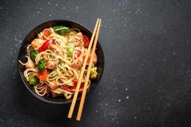 Kızarmış tavuğu sebzeyle karıştır ve siyah arka planda erişte. Asya mutfağı. Tasarım için alanı olan üst görünüm.