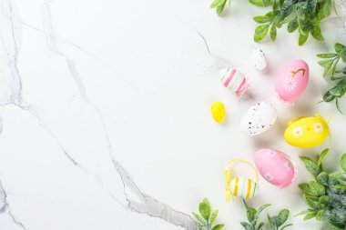 Beyaz arka planda renkli yumurtalar ve yeşil bitkilerle Paskalya kompozisyonu. Kopyalama alanı olan düz.