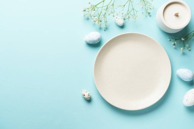 Mavi üzerine Paskalya masası. Boş tabak, çatal bıçak takımı, paskalya yumurtası ve çiçekler. Düz görünüm.