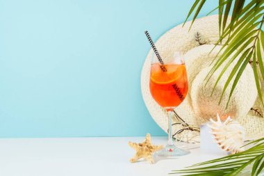 Mavi arka planda yaz tatili konsepti. Aperol Spritz, güneş gözlükleri, güneşli gölgeli şapka ve deniz kabuğu..