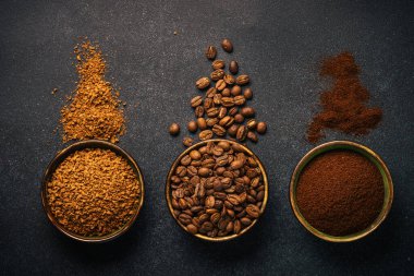 Roasted coffee beans, ground coffee and instant coffee in bowls at dark background. Top view image.